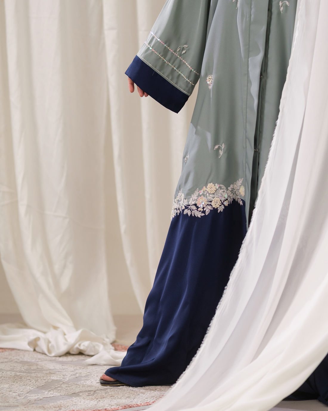 Dhaagey Artisan Weave Front-Open Abaya in Sage Green and Navy, showing scattered embroidery and dense floral border at the color block seam.