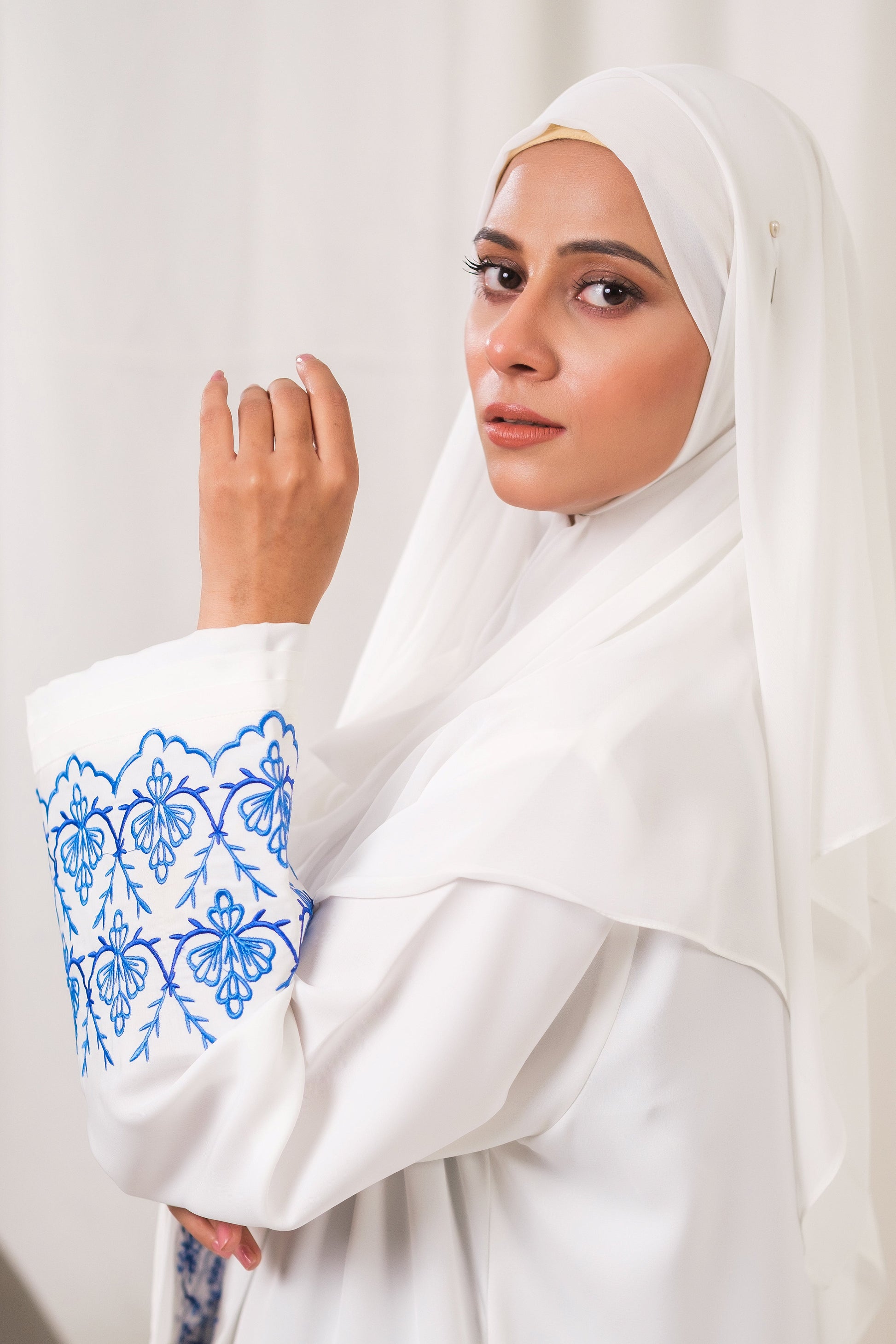 Dhaagey Isnik Motif White Front-Open Abaya in Nidha, showing the full flow and the bold Royal Blue embroidery on the wide cuffs.