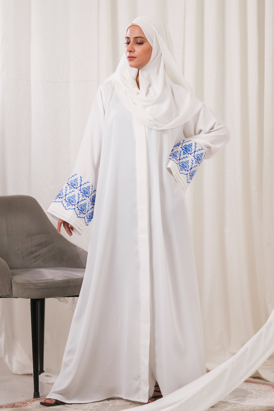 Dhaagey Isnik Motif White Front-Open Abaya in Nidha, showing the full flow and the bold Royal Blue embroidery on the wide cuffs.