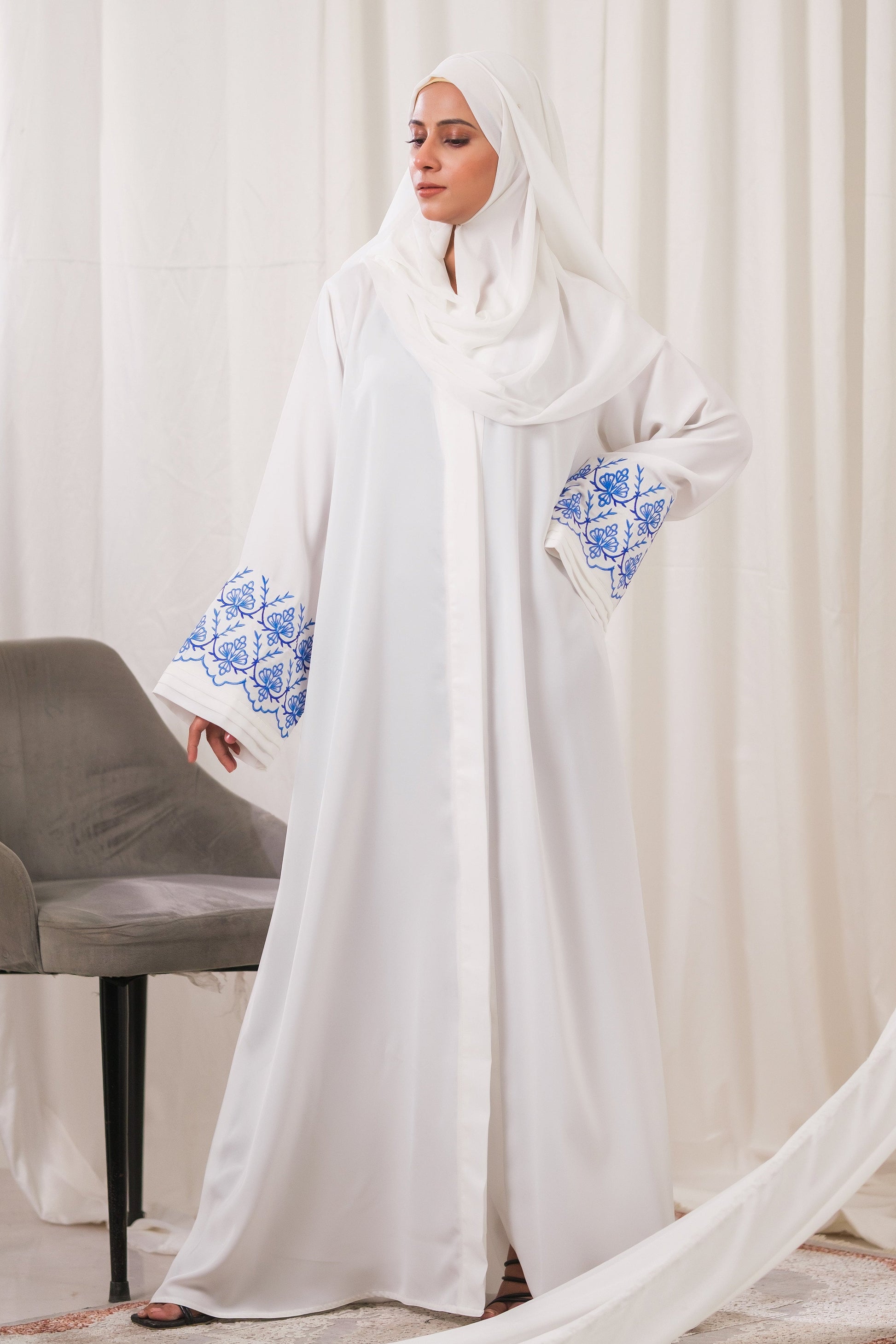 Dhaagey Isnik Motif White Front-Open Abaya in Nidha, showing the full flow and the bold Royal Blue embroidery on the wide cuffs.