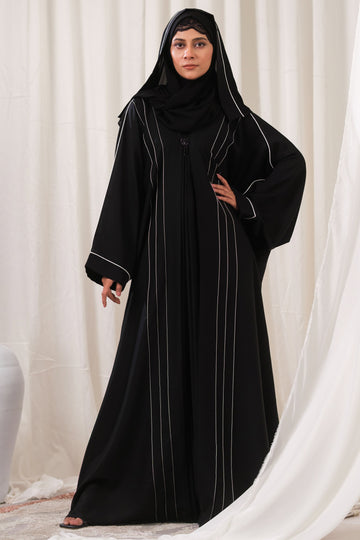 Dhaagey Meridian Abaya in black, showing the voluminous silhouette, central pleated design, curved CTC paneling with White Piping, and the black beaded ornament.