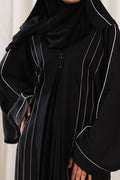 Dhaagey Meridian Abaya in black, showing the voluminous silhouette, central pleated design, curved CTC paneling with White Piping, and the black beaded ornament. Close-up