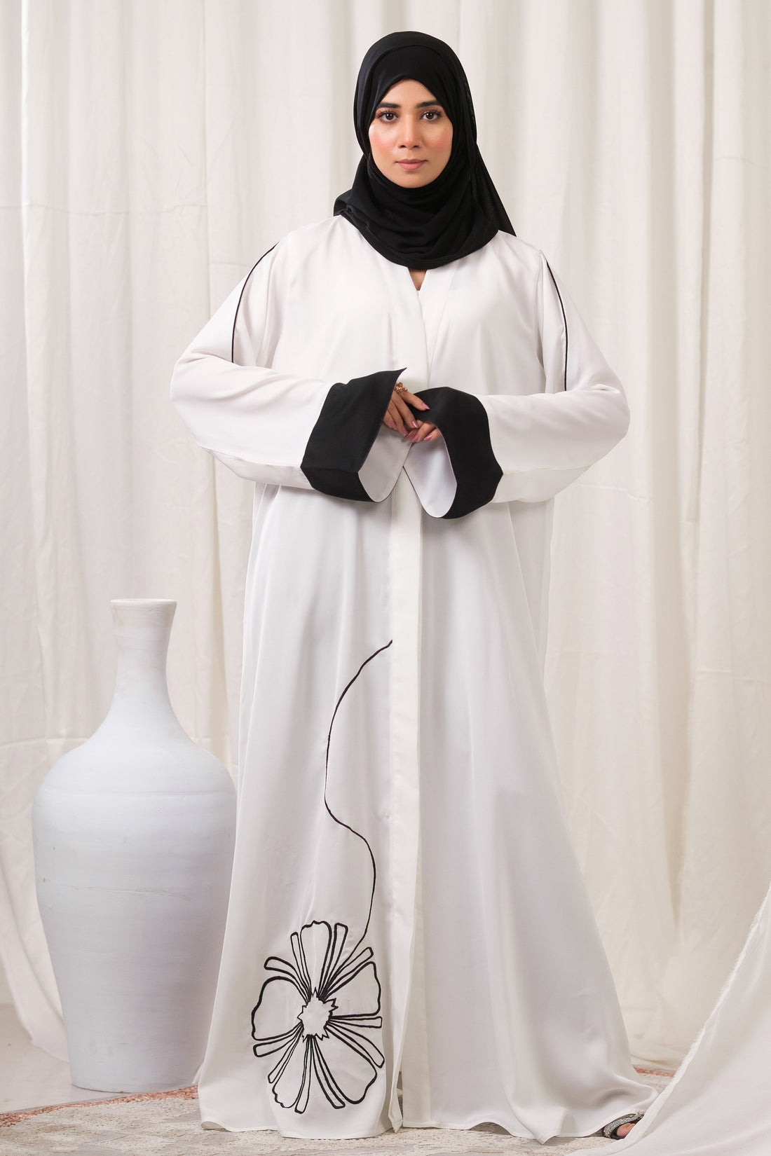Dhaagey Modern Bloom Abaya in white Imported Nidha, full length, showing black contrast trim and oversized floral appliqué near the hem.