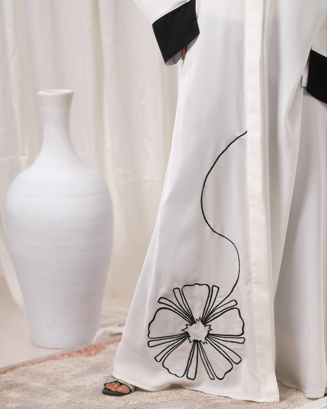 Dhaagey Modern Bloom Abaya in white Imported Nidha, full length, showing black contrast trim and oversized floral appliqué near the hem.