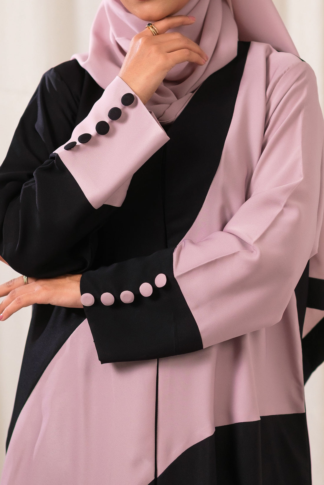 Dhaagey Intersect Abaya showing abstract curved color blocking in Black and Nude Pink with asymmetrical cuffs featuring contrasting color buttons.