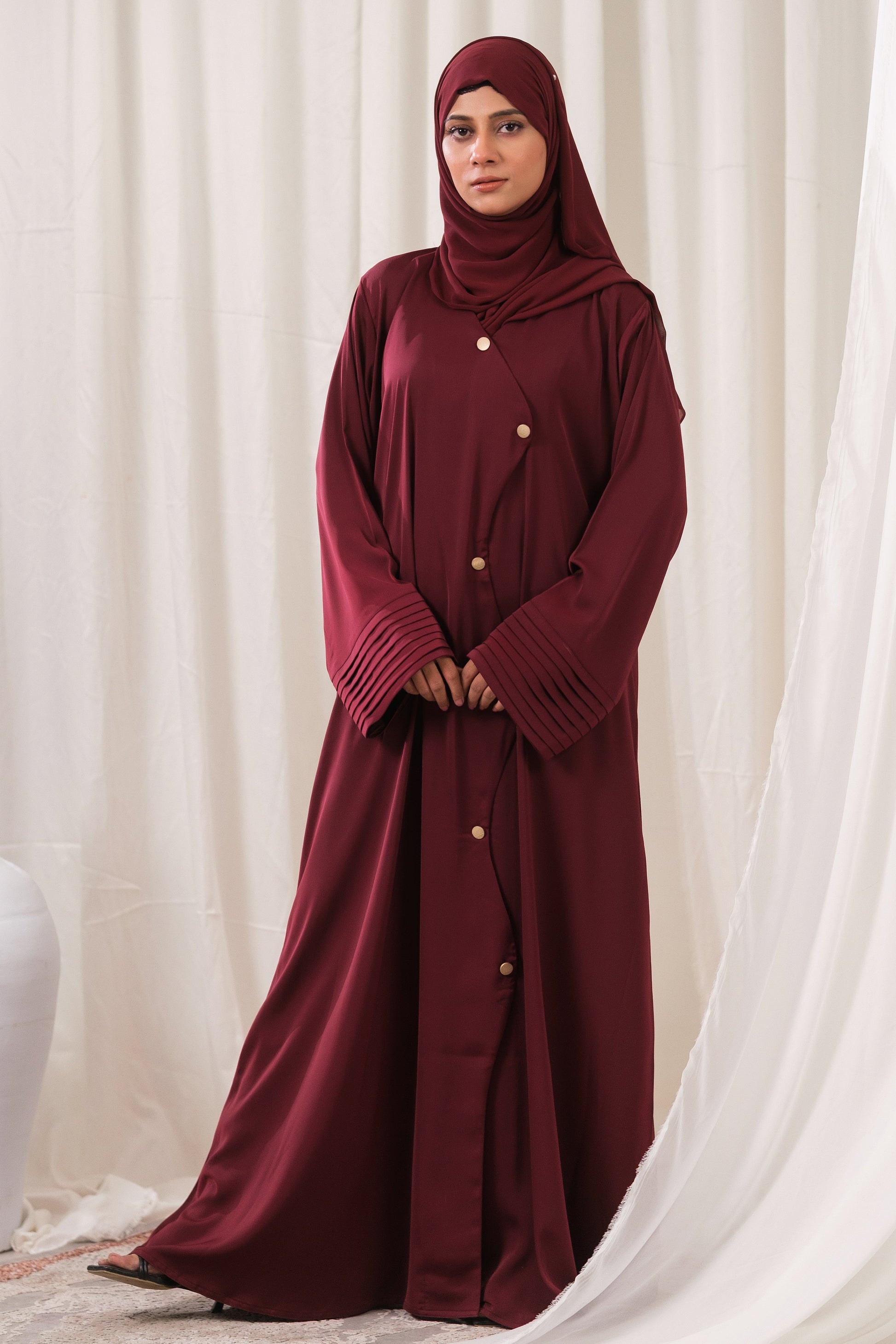 Dhaagey Regalia Front-Open Abaya in Burgundy, showing the structured fit, gold buttons, and micro-pleated bell cuffs.